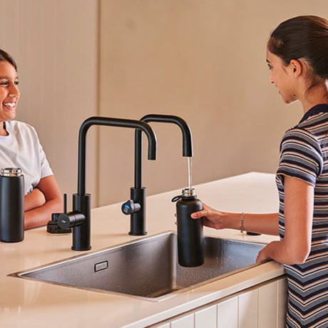 Woman actively filling a black pitcher from the HydroTap G5 Cube Plus boiling and chilled kitchen tap in a modern kitchen setting
