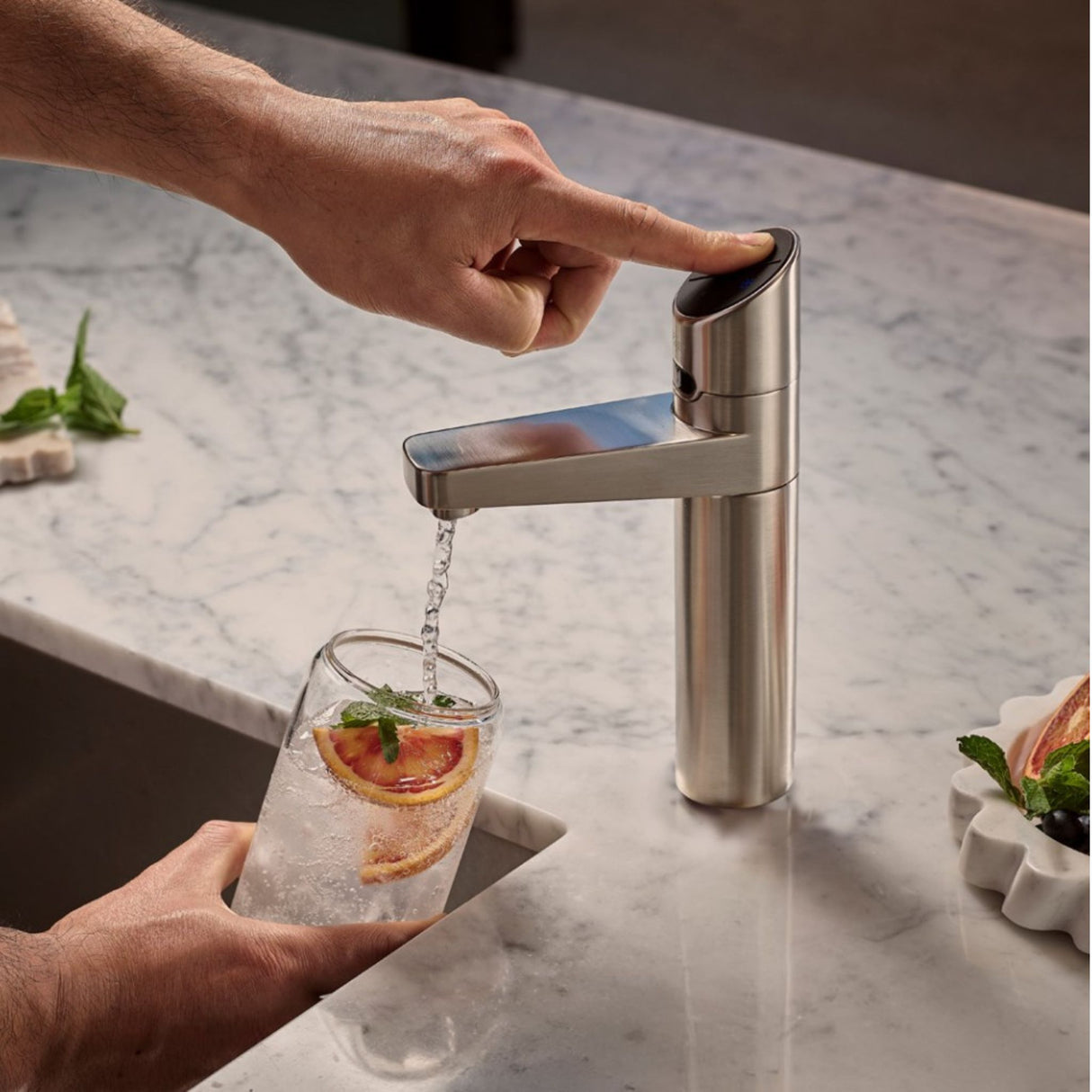 A modern single-handle kitchen faucet demonstrating ZIPS CO2 sparkling water feature with the water flowing into a glass of iced lemonade on a white marble countertop.