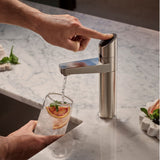 A modern single-handle kitchen faucet demonstrating ZIPS CO2 sparkling water feature with the water flowing into a glass of iced lemonade on a white marble countertop.