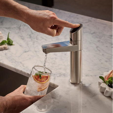 A modern single-handle kitchen faucet demonstrating ZIPS CO2 sparkling water feature with the water flowing into a glass of iced lemonade on a white marble countertop.