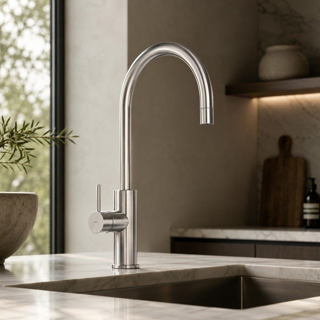 A modern high-arc chrome kitchen faucet installed on a marble countertop in a stylish kitchen setting.