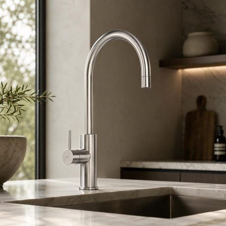 A modern high-arc chrome kitchen faucet installed on a marble countertop in a stylish kitchen setting.