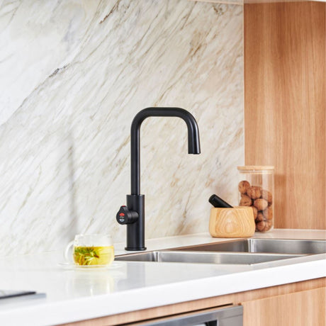 The Zip HydroTap G5 Cube Plus in matte black installed on a white countertop with a double sink, set against a marble backsplash